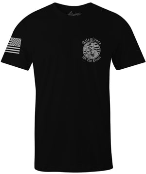 Black t-shirt with small chest print of a skull patriot wearing a tricorn hat and tactical vest, surrounded by the text 'Allegiance We The People'; right sleeve displays a forward-facing American flag